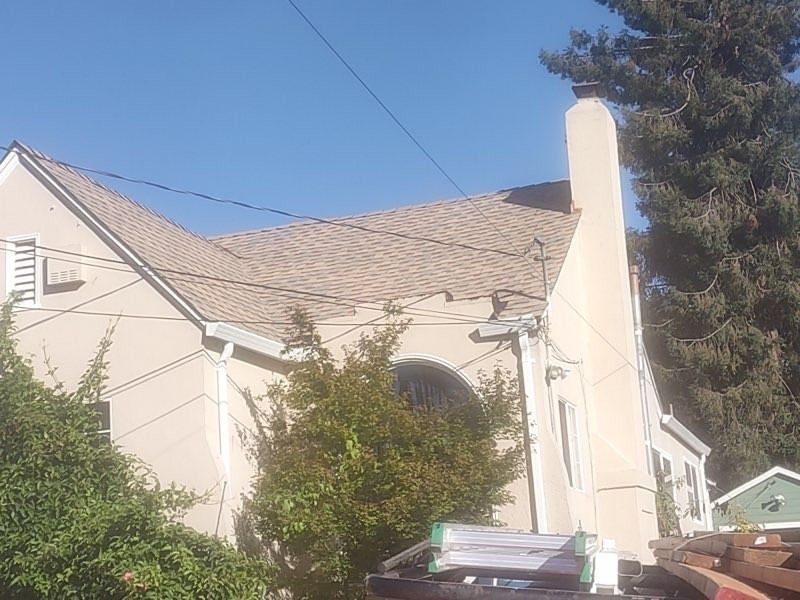 Cream-colored house with a chimney, arched window, and trees under a clear blue sky.