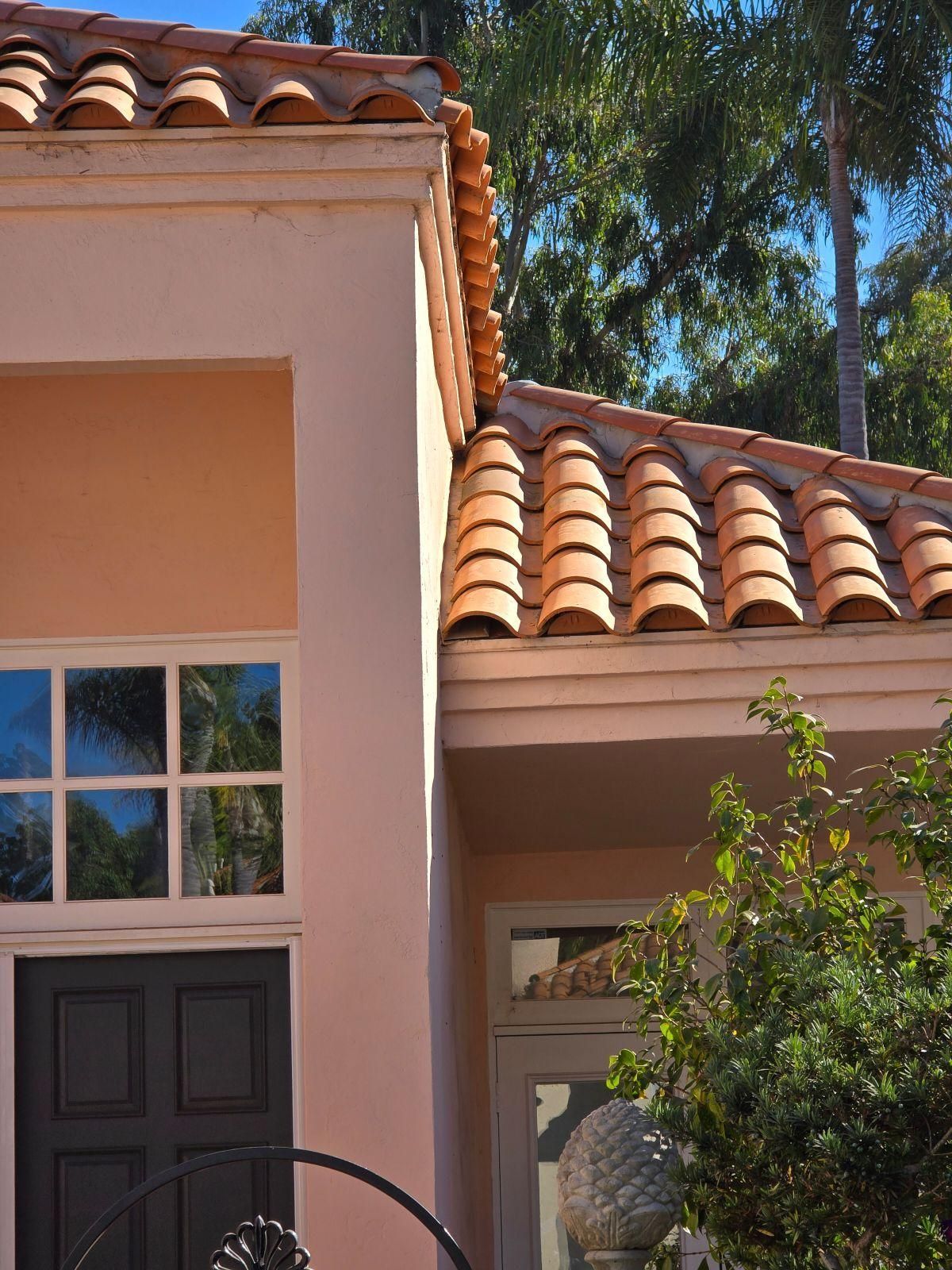 Stucco house with terracotta roof tiles, dark front door, and tall trees in the background