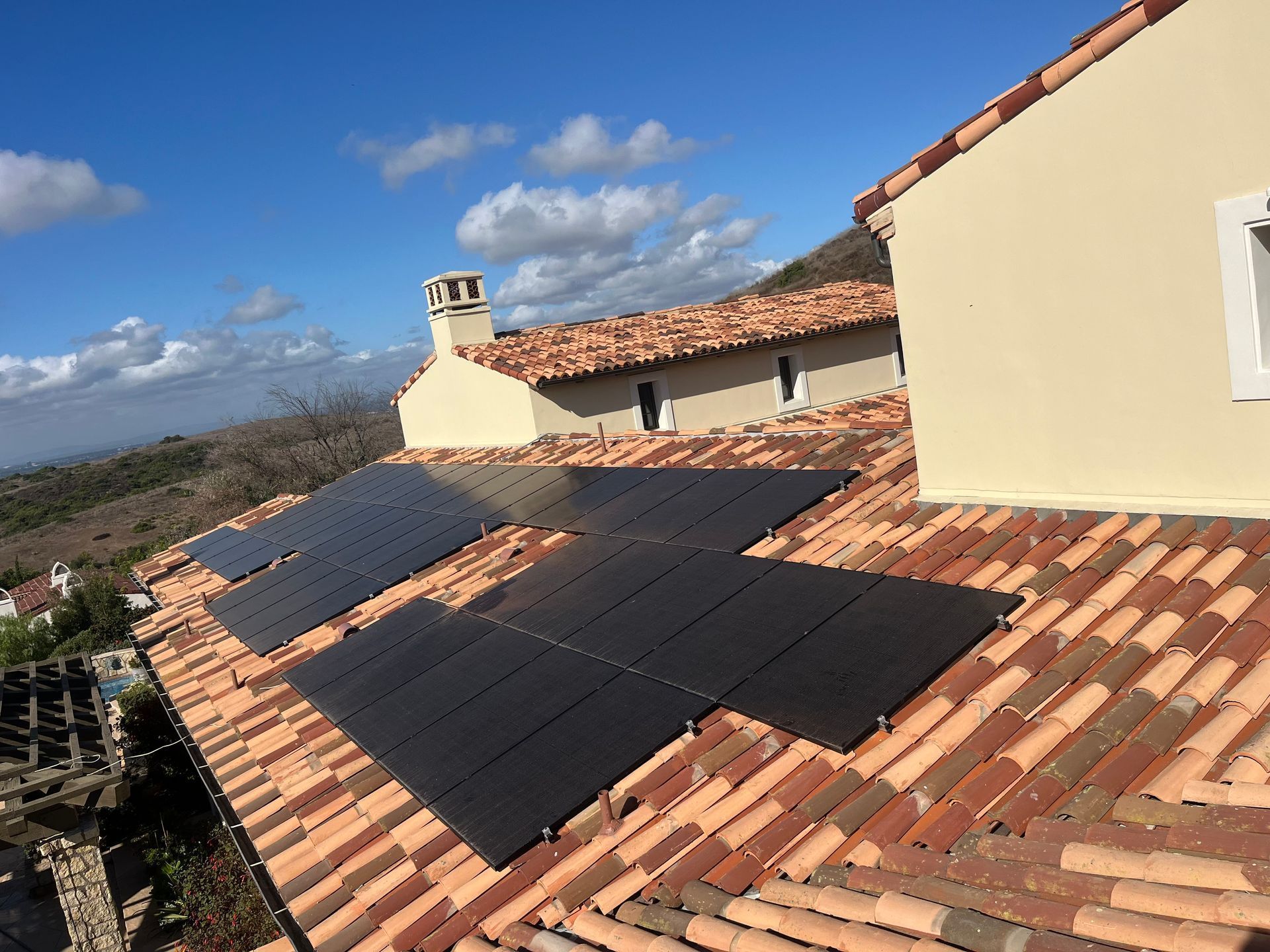 Solar panels on a red-tiled roof beside a cream house under a blue sky