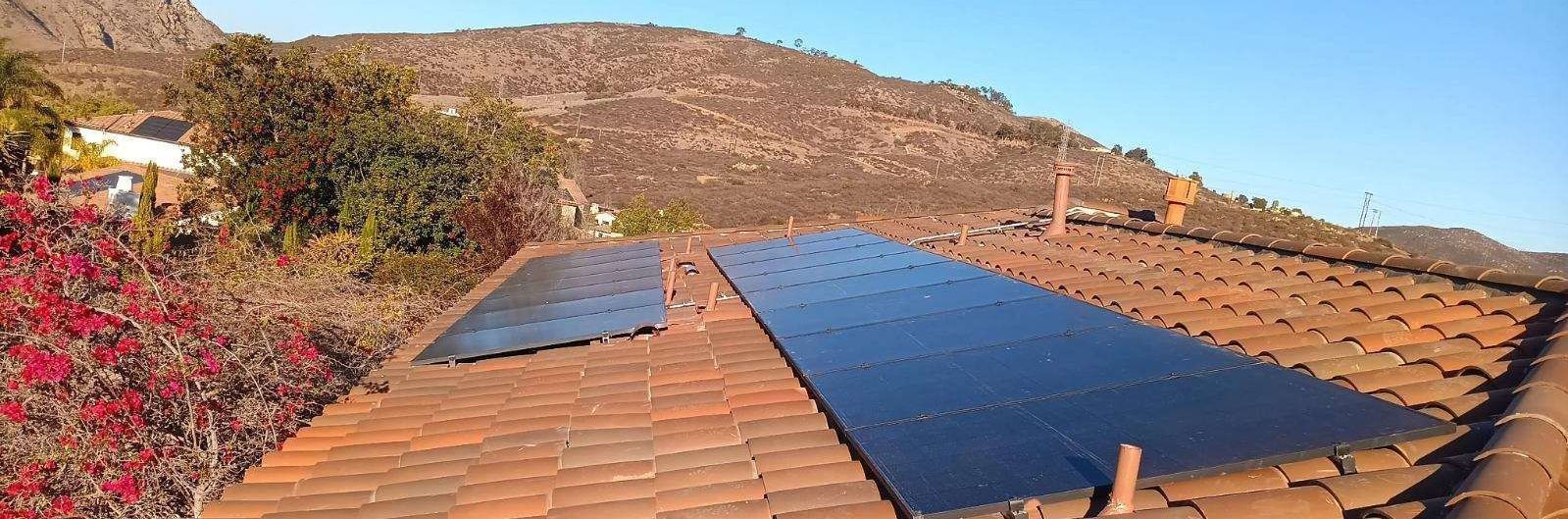 Rooftop solar panels on a terracotta-tiled roof with hills and clear sky in the background
