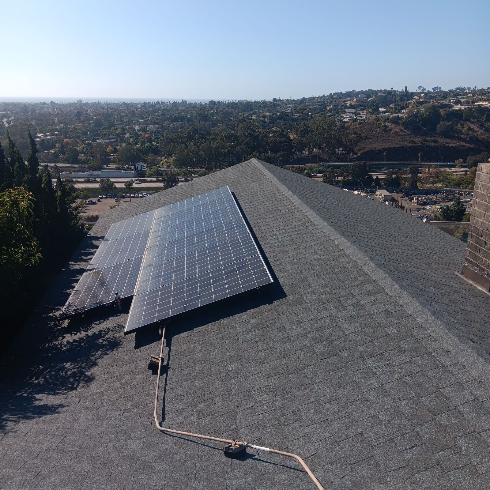 Solar panels on a gray shingle roof overlooking a distant suburban valley