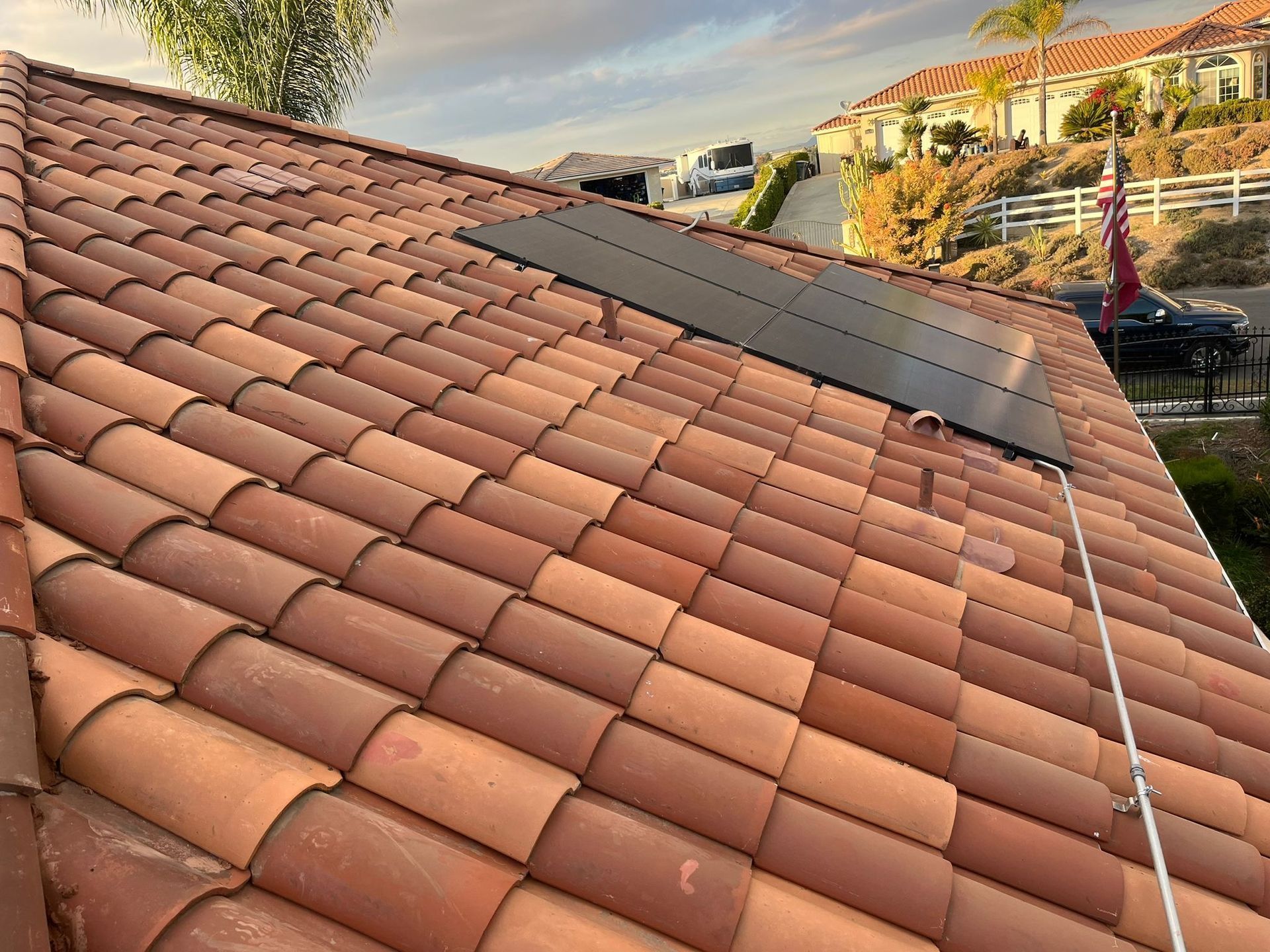 Terracotta tile roof with black solar panels on a hillside home at sunset