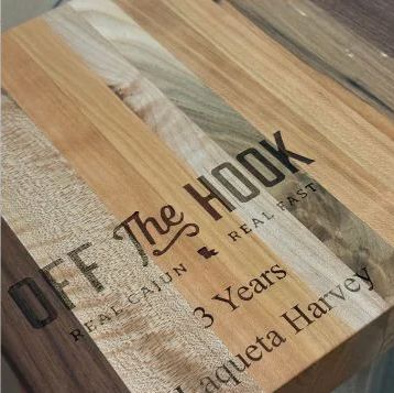 Wooden plaque with engraved black text reading 'Off the Hook' and '3 Years' on a striped wood background