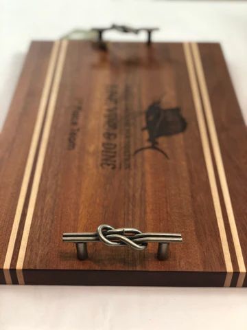 Wooden serving board with light stripes and metal handles, engraved with a tree and text.