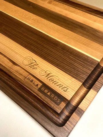 Wooden cutting board with dark handle and engraved logo, on a light surface.