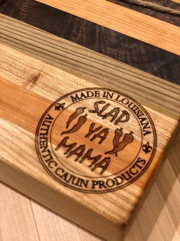 Round 'Ya Mama' Authentic Cajun Products logo on a wooden cutting board.