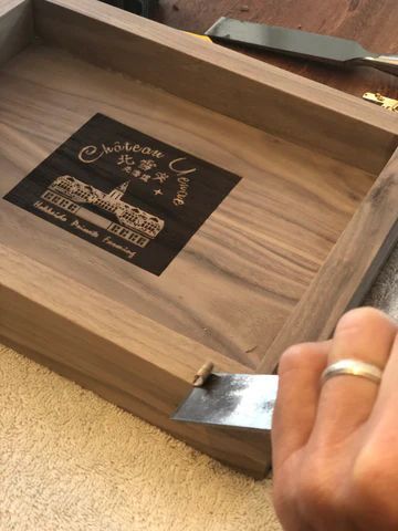 Hand placing a metal bracket into a wooden box with a branded label inside.