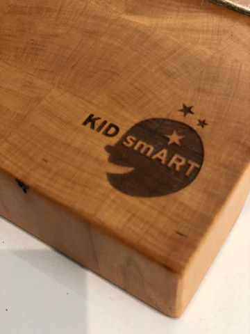 Close-up of a wooden block with a dark 'KID SMART' logo and star design burned into it.