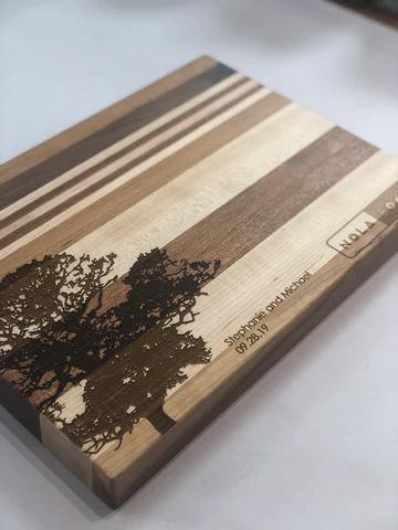 Wooden cutting board with striped wood grain and a black tree silhouette engraving