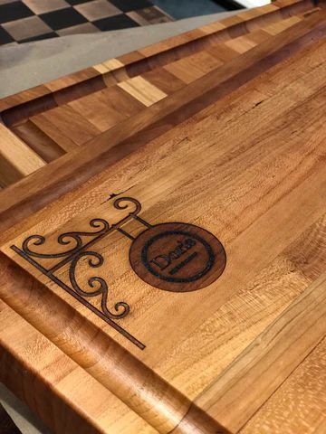 Wooden tabletop with a decorative dark scrollwork logo burned into one corner.
