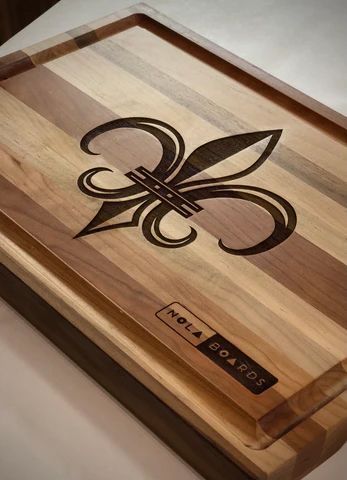 Wooden cutting board with a fleur-de-lis inlay and a small nameplate on the corner.
