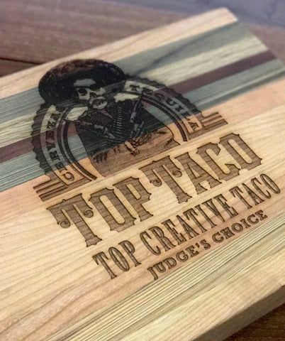 Wooden cutting board with engraved 'TOP TACO' logo and text in dark brown and black.