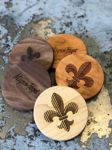 Four round wooden coasters with engraved fleur-de-lis designs in brown and gold tones