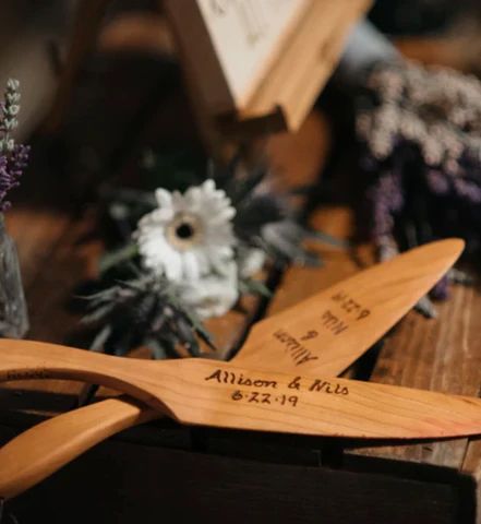 Wooden decorative airplane with engraved names on a rustic table, surrounded by flowers