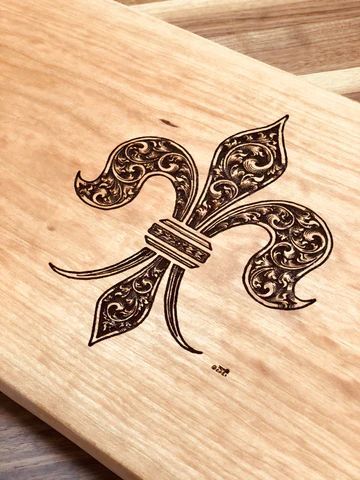 Laser-etched fleur-de-lis design on a light wood surface.