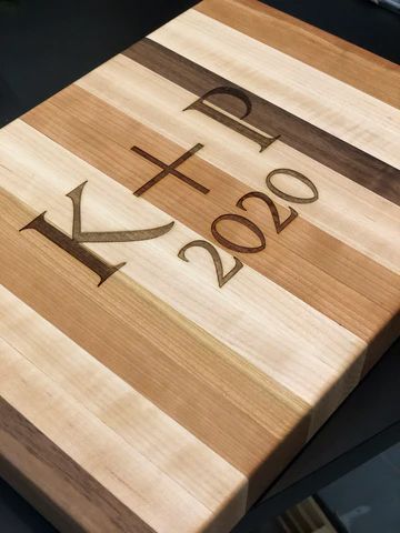 Wooden cutting board with engraved 'K+ 2020' on a striped wood grain surface.