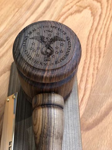 Wooden gavel-style handle with a round engraved top on a wood-grain background