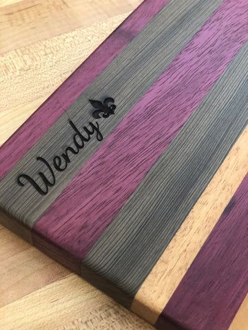 Personalized wooden cutting board with multicolored stripes and the name 'Wendy' engraved