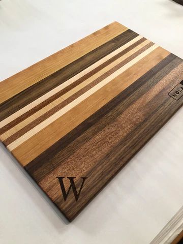 Wooden striped cutting board with engraved initials on a white surface.