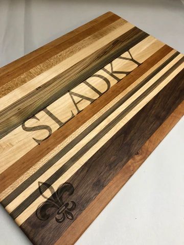 Wooden cutting board with striped grains, engraved 'SLEEKY,' and a fleur-de-lis design