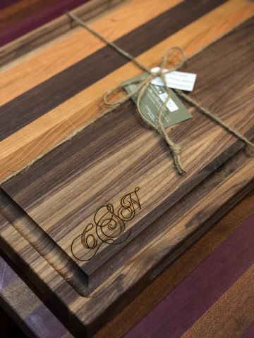 Engraved wooden cutting board with a ribbon tied around it on a striped tabletop.