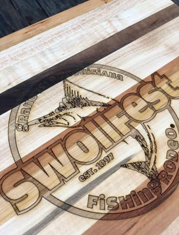 Laser-engraved circular 'SMWFest Fishing' logo on a wooden board, with a fish and rod graphic.
