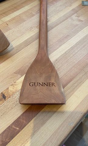 Wooden paddle labeled 'GUNNER' resting on a striped wooden countertop.