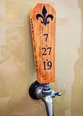 Wooden tap handle with fleur-de-lis and numbers 7, 27, 19 on a beer tap