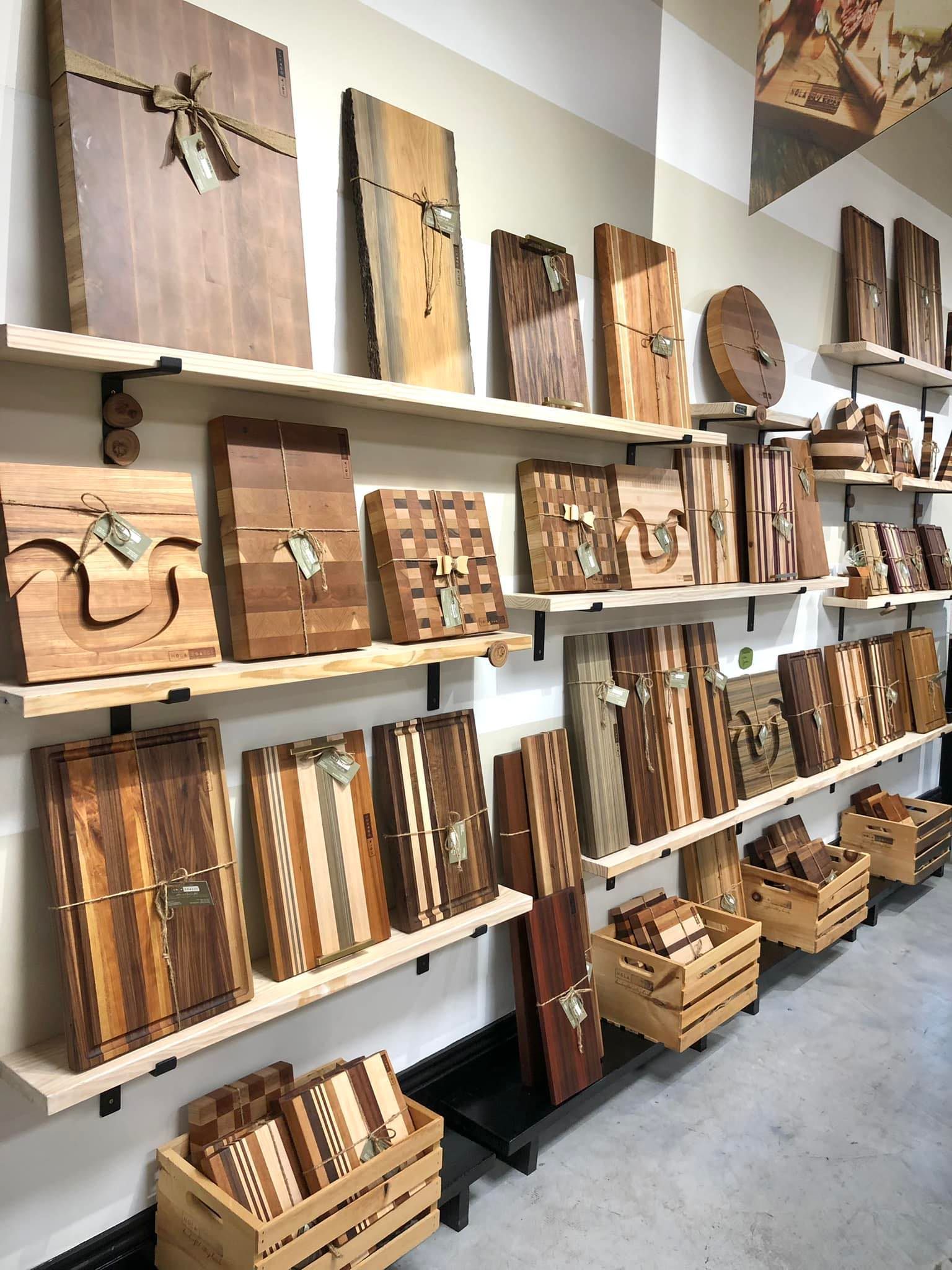 Shelves in a shop display various handmade wooden cutting boards, serving trays, and small crates of wood products.