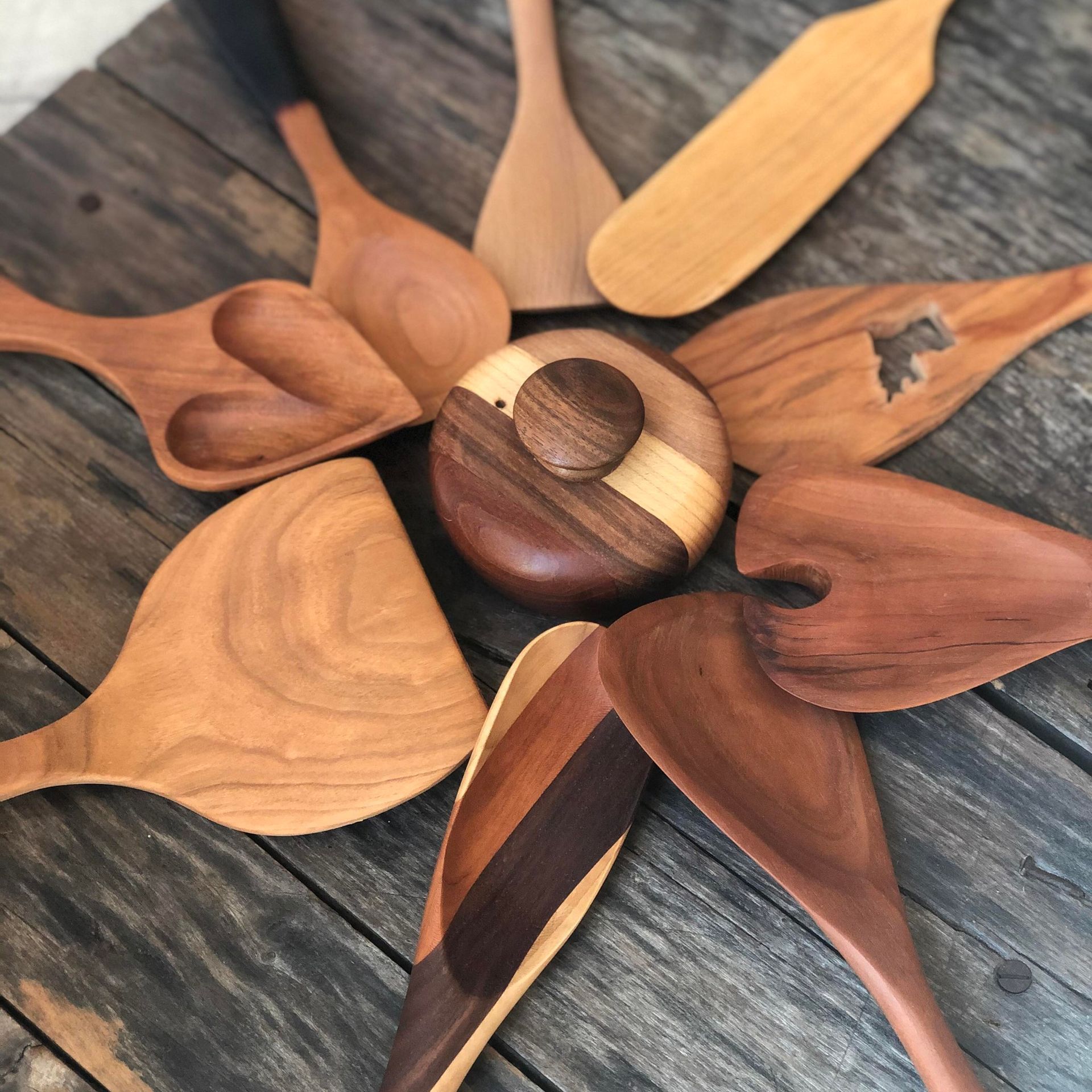 A circular wooden knob sits surrounded by various handcrafted wooden kitchen spatulas and spoons on a rustic table.