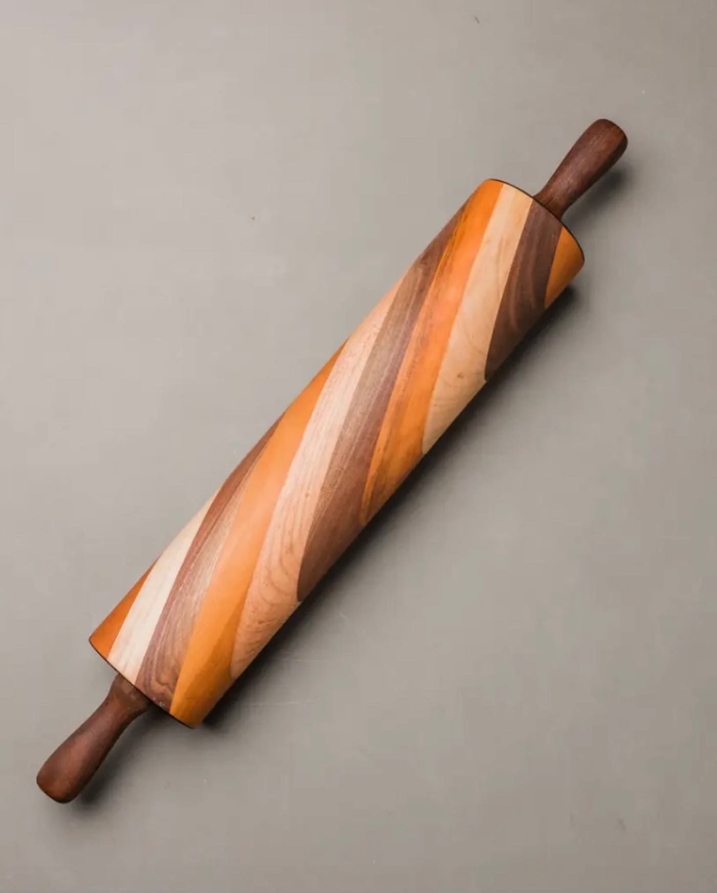 A multi-toned wooden rolling pin featuring a diagonal striped pattern, centered against a plain gray background.