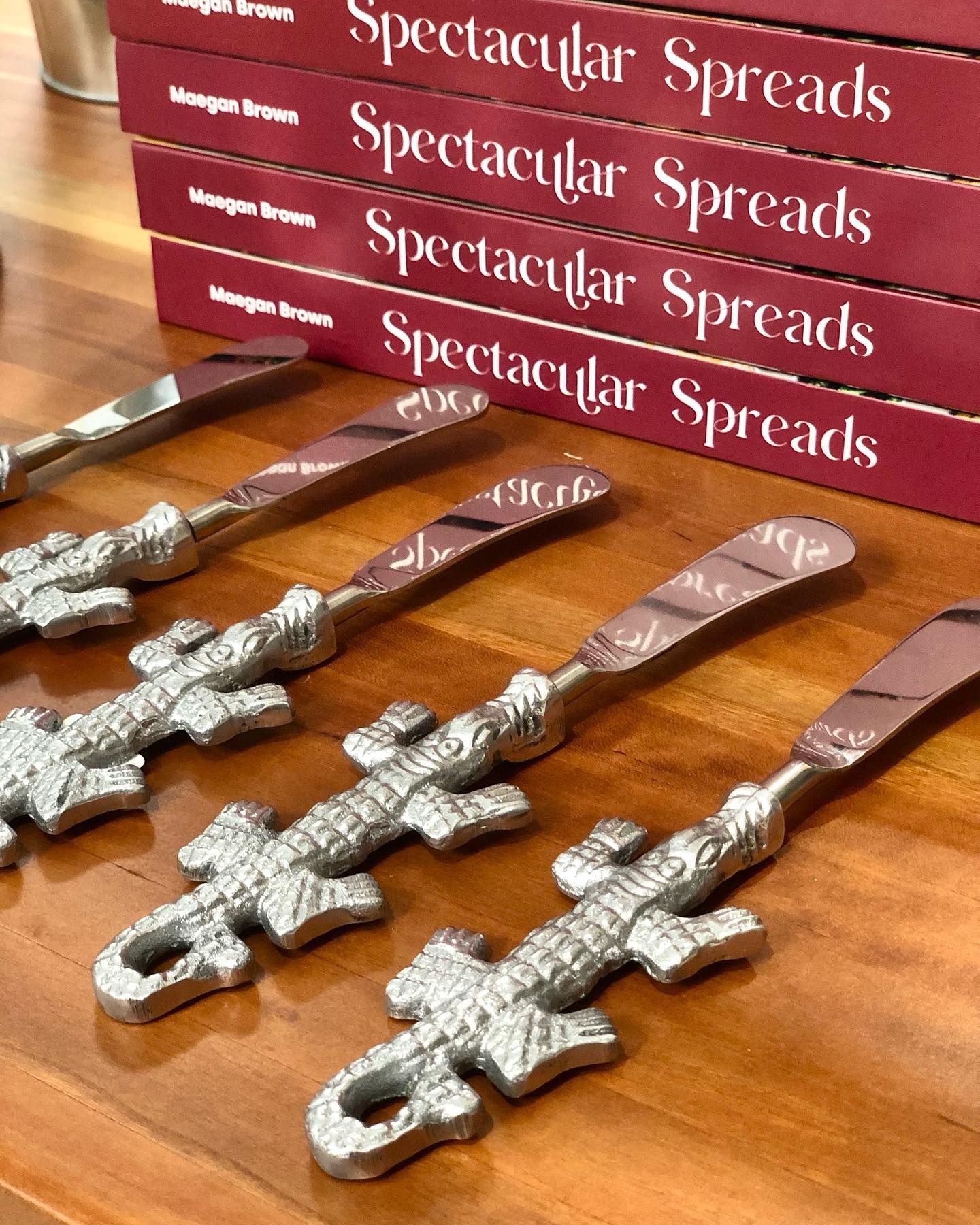 Four spreaders arranged diagonally on a wooden table in front of a stack of Spectacular Spreads books.