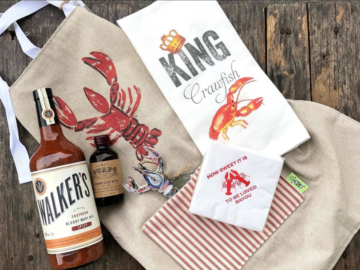 A crawfish boil set including a large metal pot, wooden paddle, and seasoning packet, displayed on a wooden surface.