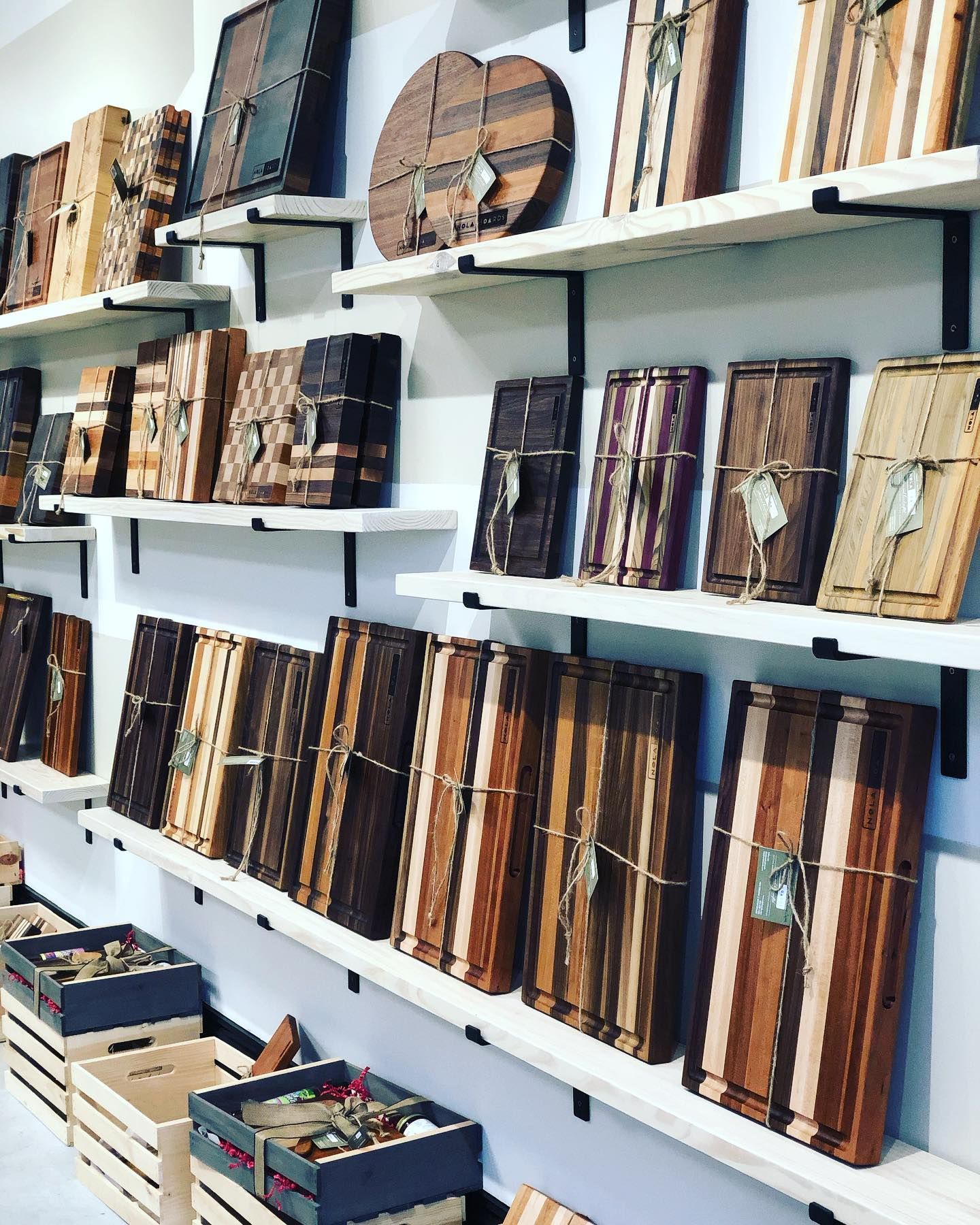 Shelves display a variety of handmade wooden cutting boards in different shades, stripes, and sizes, with crates below.