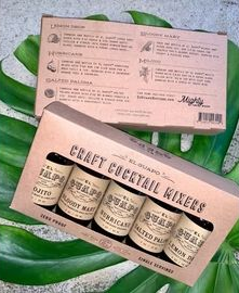 Pink gift box with three cocktail mixer bottles on green leaves and a matching card box above