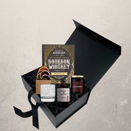 Black gift box with bourbon whiskey set, including bottles, snacks, and a label on a light background
