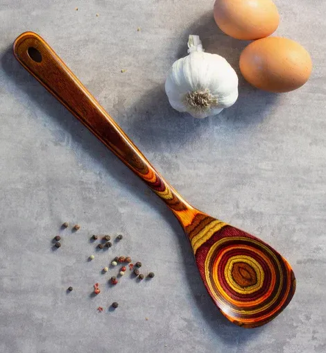 A wooden spoon sits on a table next to eggs and garlic
