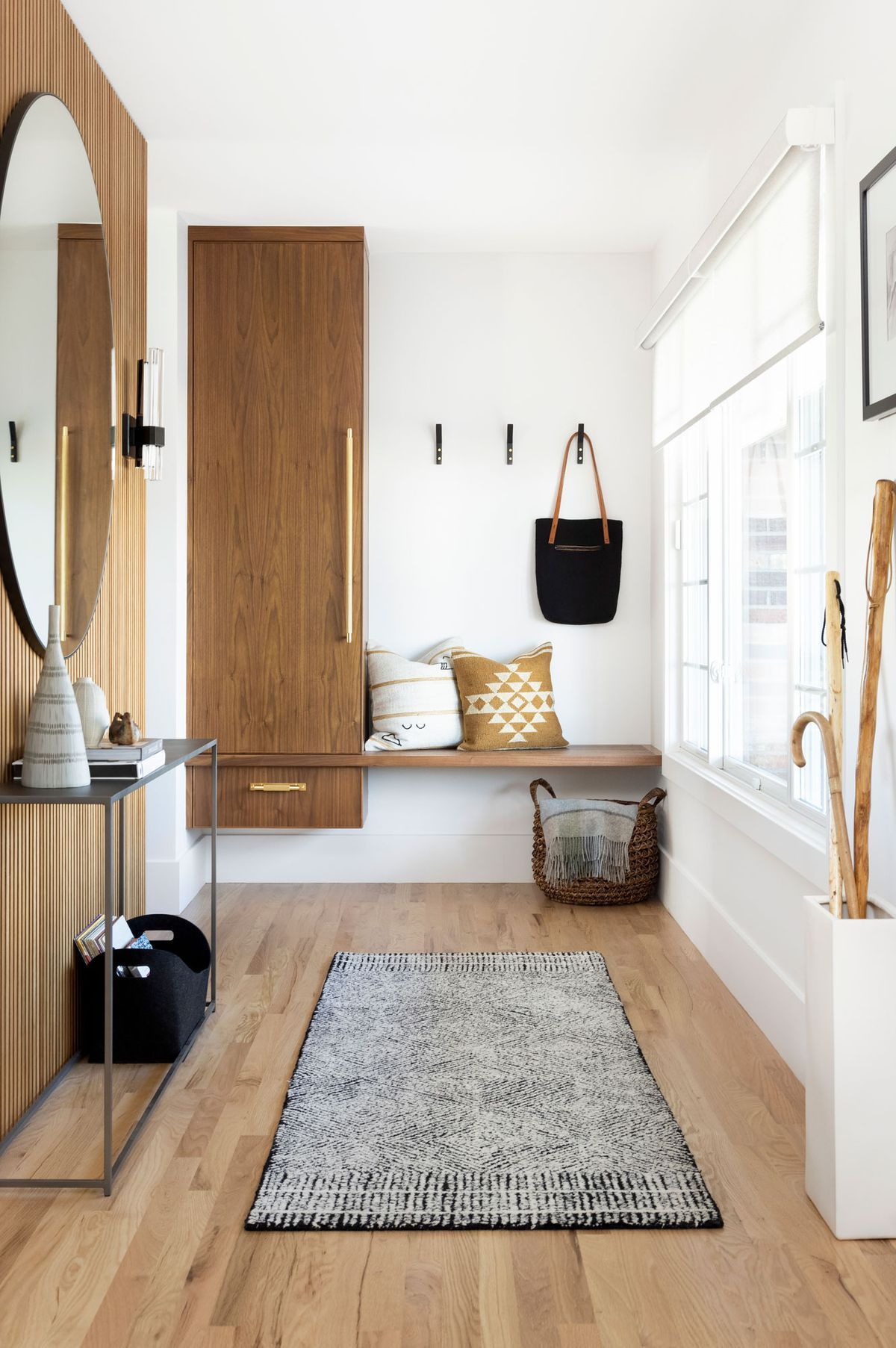 A hallway with hardwood floors, a rug, a mirror, and a bench.