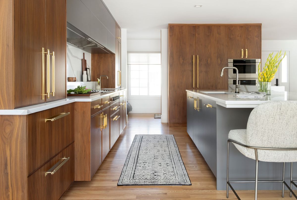 A kitchen with wooden cabinets, stainless steel appliances, a rug, and a chair.