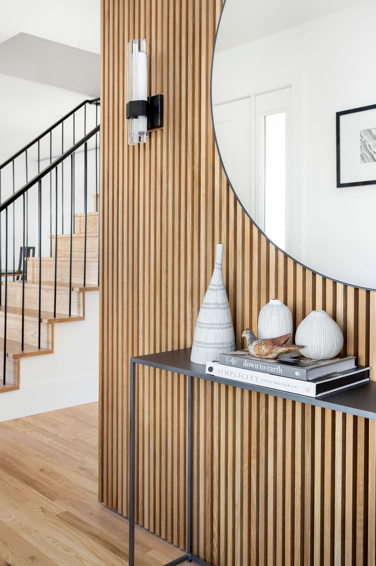 A hallway with a wooden wall, a table, a mirror, and stairs.