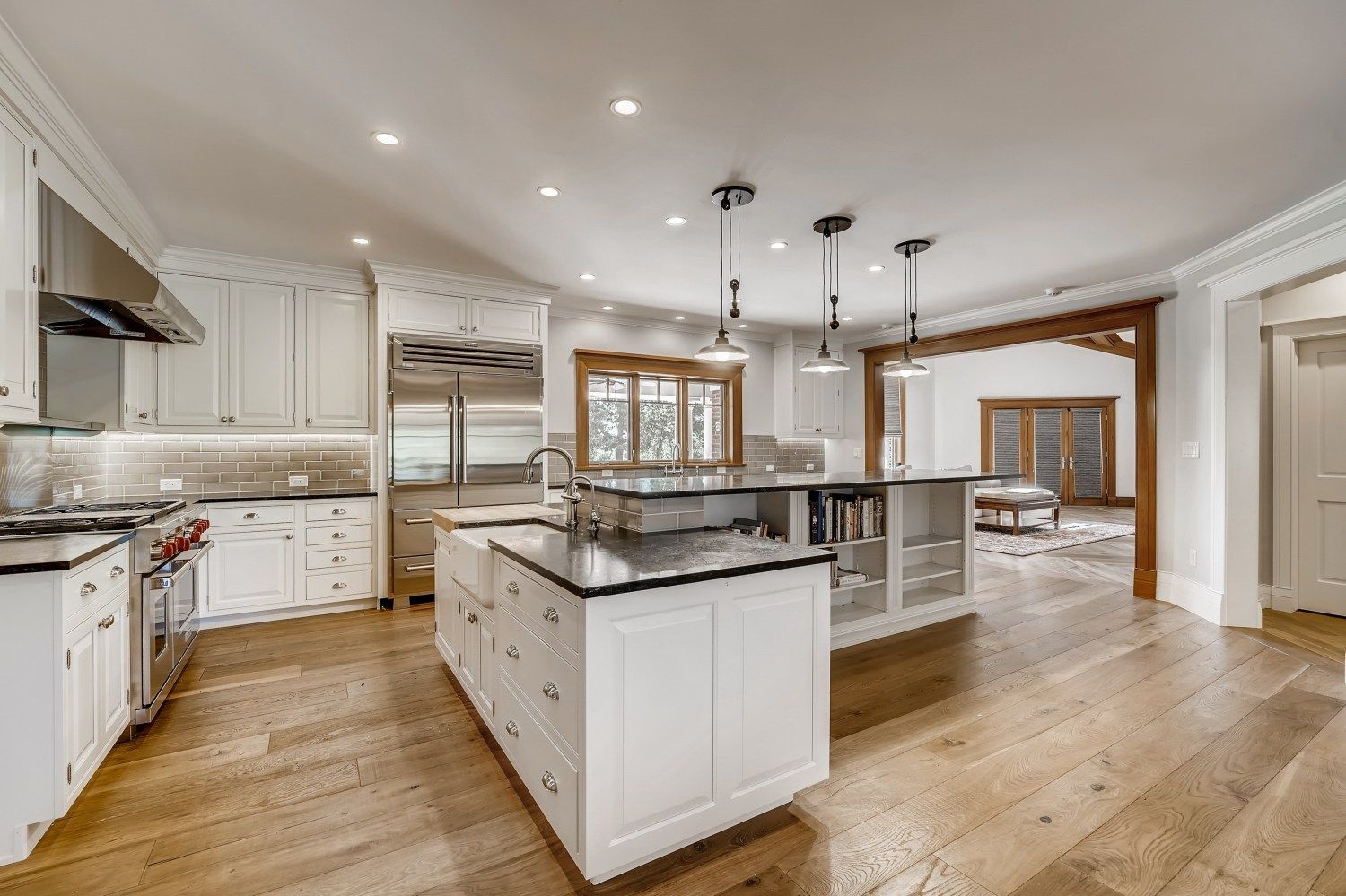 A kitchen with white cabinets, black counter tops, stainless steel appliances, and hardwood floors.