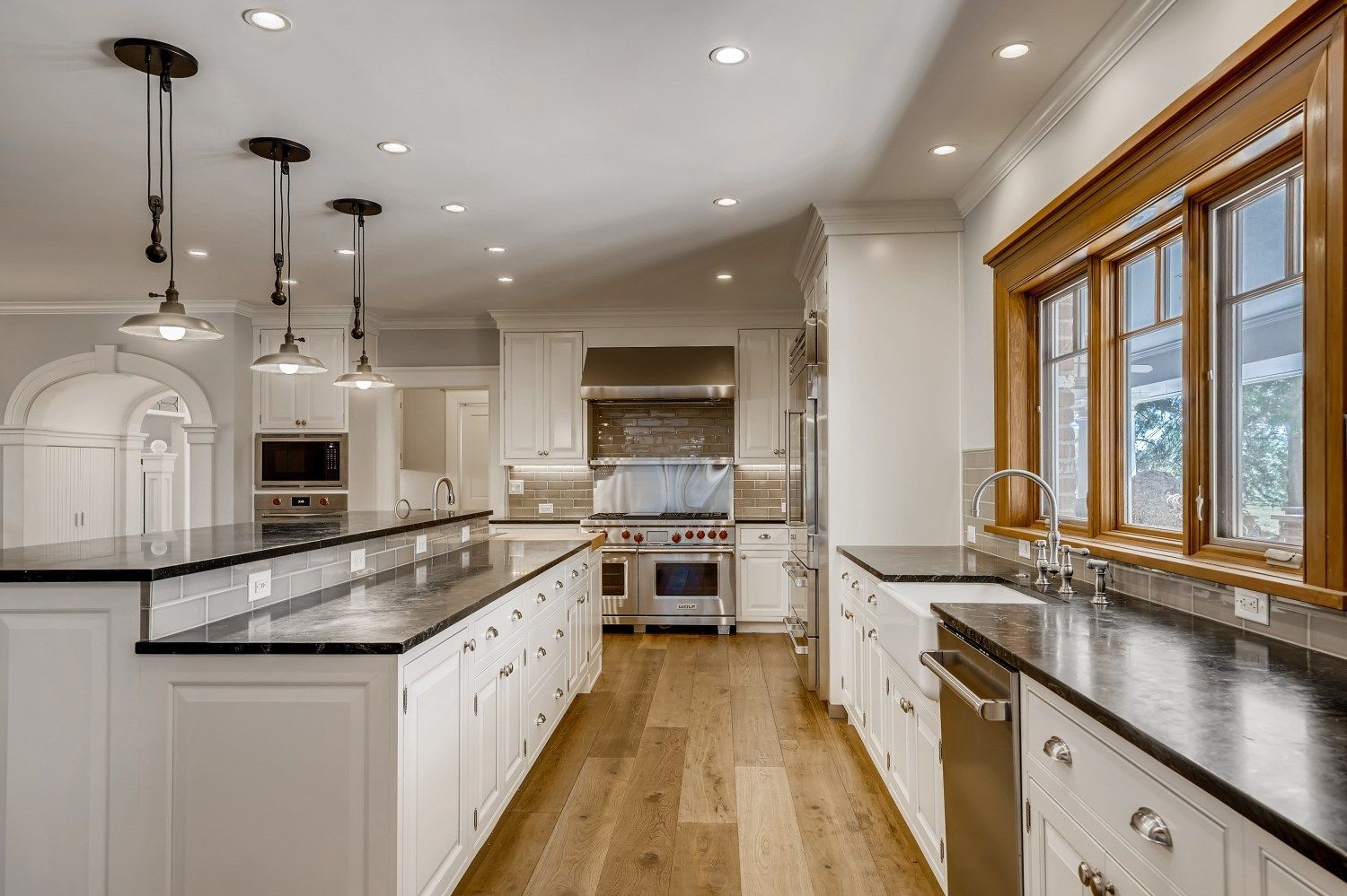 A kitchen with white cabinets, black counter tops, stainless steel appliances, and hardwood floors.