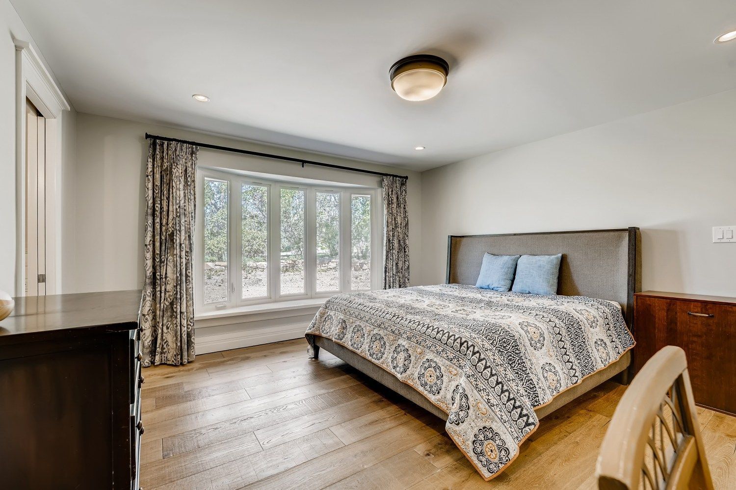 A bedroom with a large bed, dresser, chair, and window.