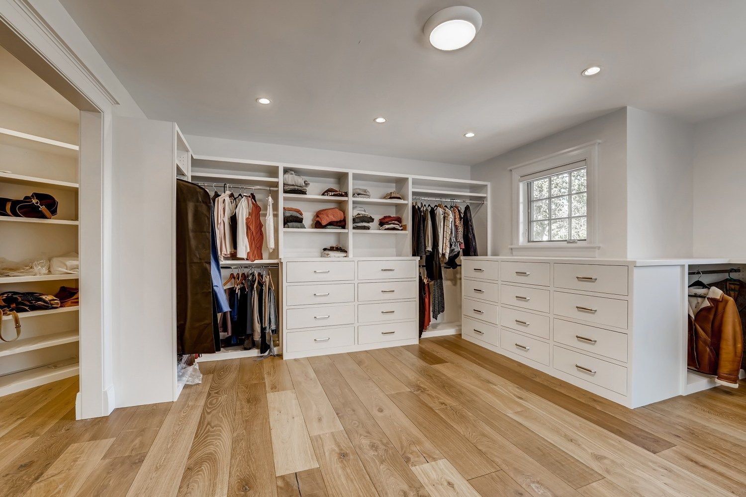 A large walk in closet with hardwood floors and white cabinets.