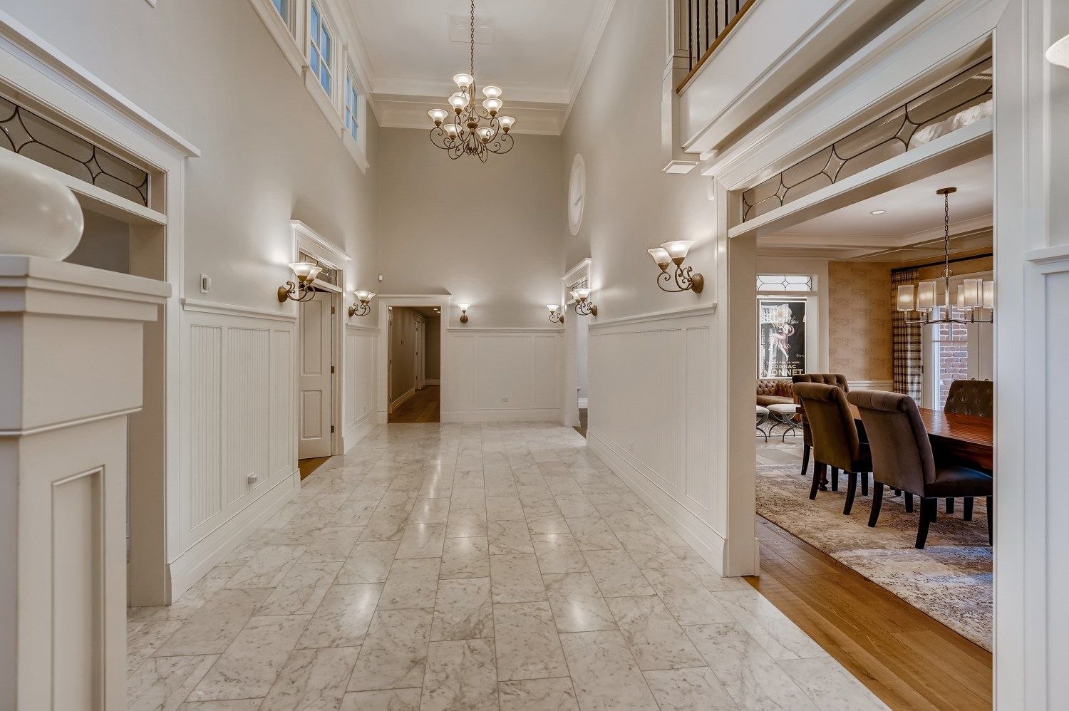 A long hallway in a house with marble floors and a chandelier hanging from the ceiling.