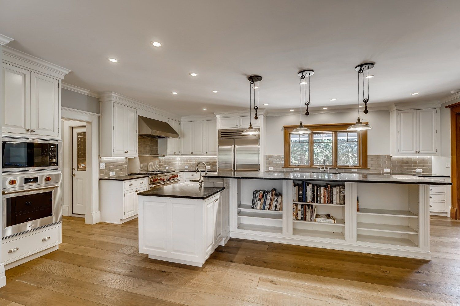 A large kitchen with white cabinets, hardwood floors, stainless steel appliances, and a large island.