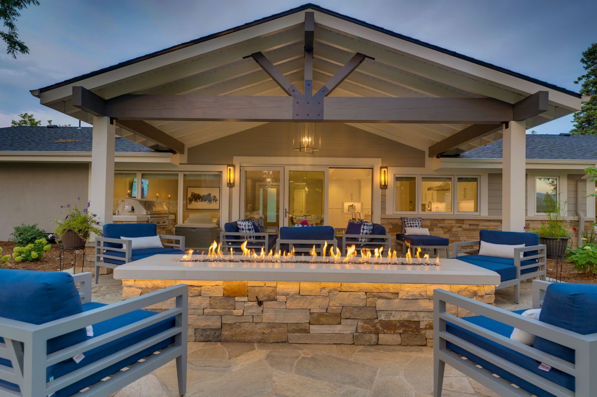 A patio with a fire pit and chairs in front of a house.