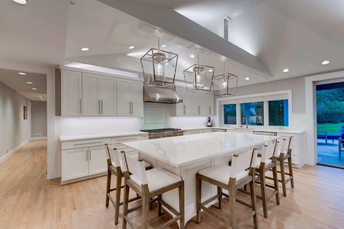 A kitchen with white cabinets, a large island, and stools.