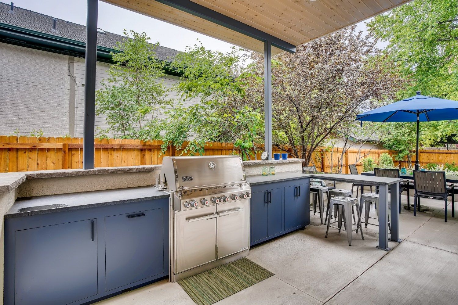 A patio with a grill, tables and chairs, and a blue umbrella.