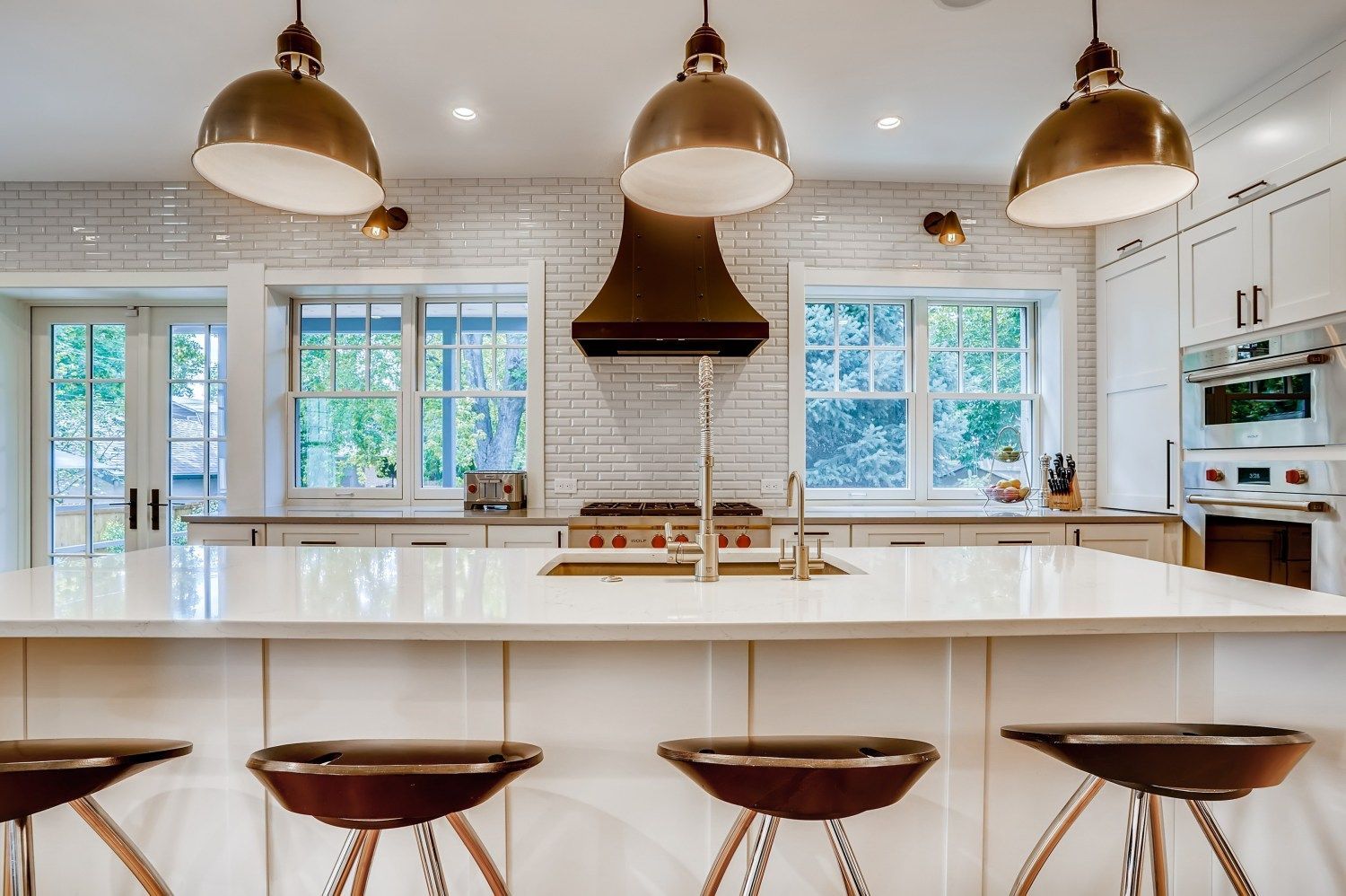 A kitchen with a large island, stools, and a stove.